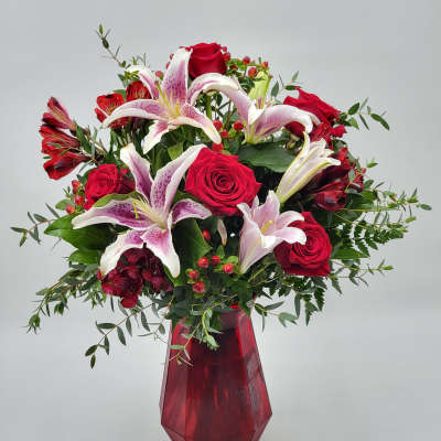 Bouquet of red roses and pink lilies in a red glass vase