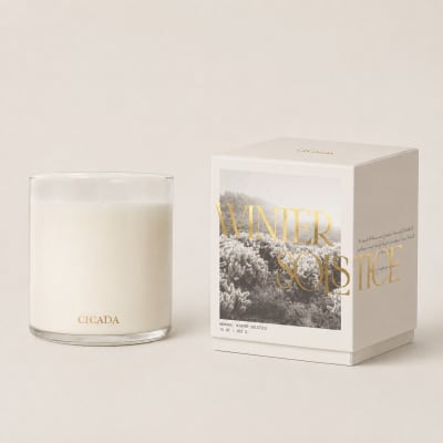 White candle in a clear glass jar beside a boxed candle set