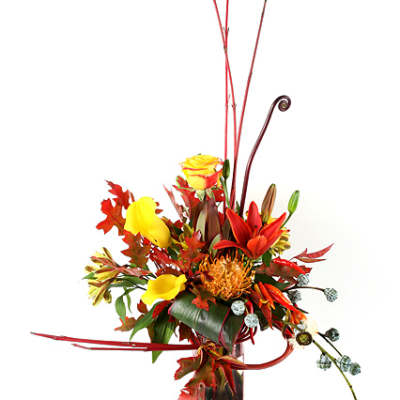 Tall autumn bouquet with yellow roses and orange lilies in a glass vase