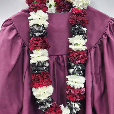 Red, white, and black carnation lei draped over a mauve graduation gown on a wooden hanger