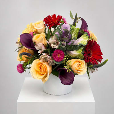 Mixed bouquet in a white vase with yellow roses, red gerberas, and purple calla lilies