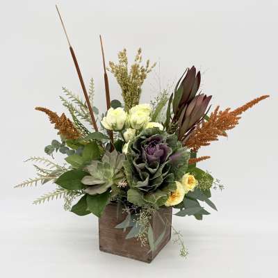 Mixed floral arrangement in a wooden box with purple and cream blooms