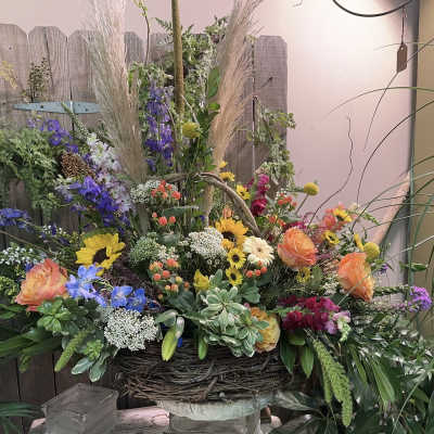 Large mixed floral arrangement in a woven basket with tall grasses and bright blooms