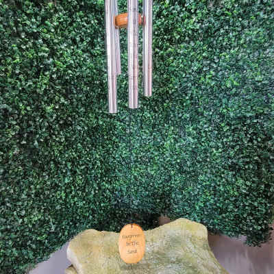 Wind chime hanging before a green foliage wall above a stone memorial marker