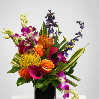 Colorful tropical bouquet in a square glass vase with orange roses and purple orchids