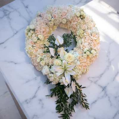 Heart-shaped floral wreath of cream roses and white lilies on a marble surface