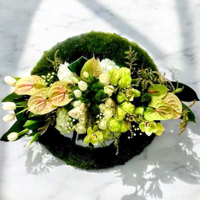 Green and white floral arrangement with anthuriums and roses on a moss base