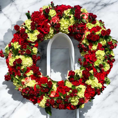 Circular floral wreath of red roses and pale green hydrangeas on a white stand