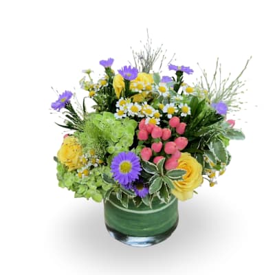 Mixed bouquet with yellow roses, purple daisies, and small white flowers in a green vase