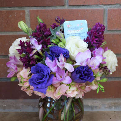 Round vase arrangement with purple, pink, and white flowers in a clear vase with branches inside