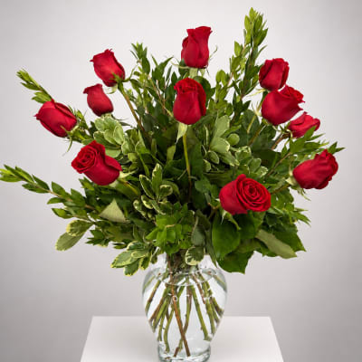 Red roses arranged in a clear glass vase with mixed greenery
