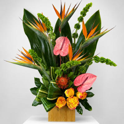 Tropical floral arrangement with pink anthuriums and bird of paradise in a wooden vase