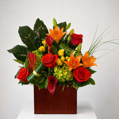 Tropical arrangement with red roses, orange lilies, and calla lilies in a wooden box