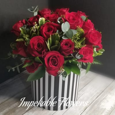 Round arrangement of red roses in a black and white striped cylinder box