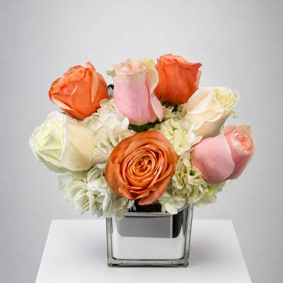 Bouquet of orange, pink, and white roses in a square glass vase