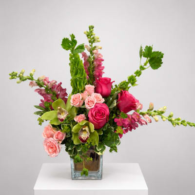 Pink roses and snapdragons arranged in a square glass vase