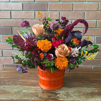 Mixed bouquet in an orange basket with roses, calla lilies, and marigolds