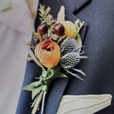 Orange and yellow boutonniere with berries and thistle on a dark suit lapel