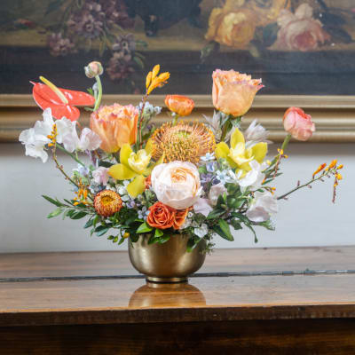 Mixed floral arrangement in a gold vase with orange, yellow, and white blooms