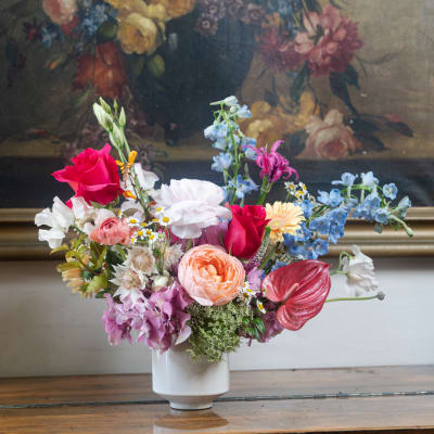 Mixed bouquet of roses, hydrangea, and delphinium in a white vase