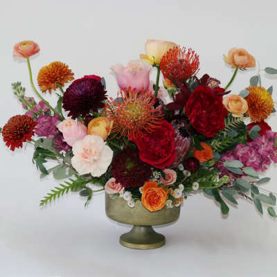 Mixed bouquet in a green pedestal vase with red, pink, and orange blooms