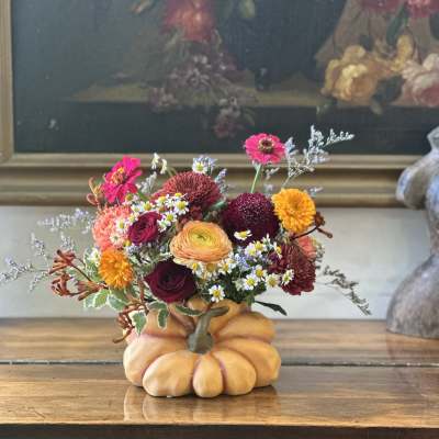Autumn-toned flower arrangement in a pumpkin-shaped container on a wooden table