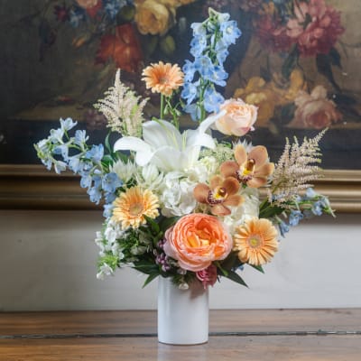 Mixed bouquet in a white vase with lilies, gerberas, roses, and blue delphinium