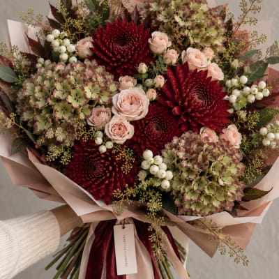 Bouquet of burgundy dahlias, blush roses, and green hydrangeas wrapped in pink paper