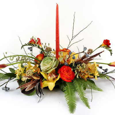 Low floral centerpiece with red candle, orange and yellow blooms, and fern accents