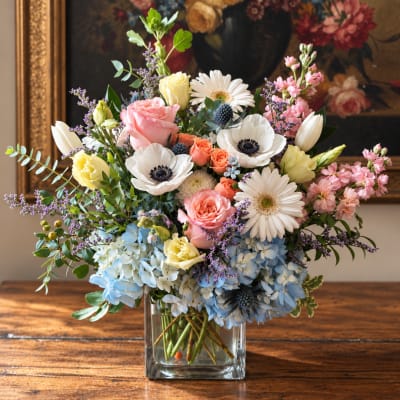 Mixed bouquet in a clear square vase with roses, daisies, and hydrangeas