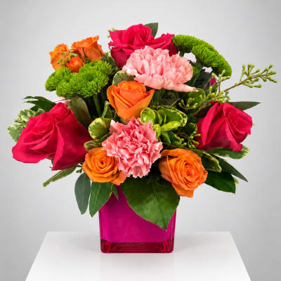 Bright mixed bouquet of roses, carnations, and green mums in a pink vase