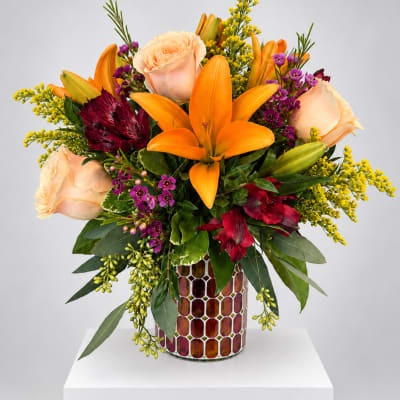 Orange lilies and peach roses in a mosaic vase