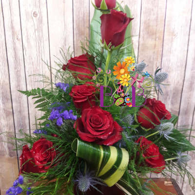 Red roses arranged in a tall vase with purple filler flowers and green ribbon accents