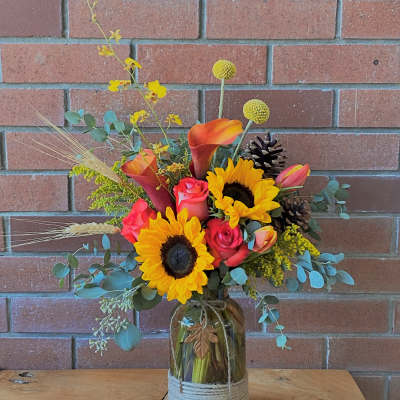 Mixed bouquet in a glass jar with sunflowers, calla lilies, and roses