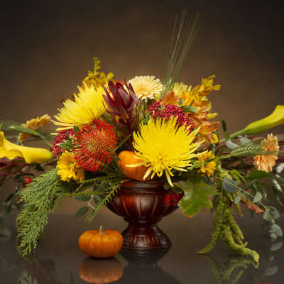 Autumn floral arrangement with yellow blooms in a dark vase and small pumpkins