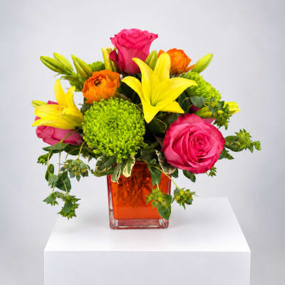 Bright mixed bouquet of roses, lilies, and green chrysanthemums in an orange vase