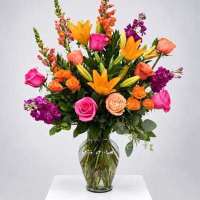Bright mixed bouquet with roses, lilies, and purple blooms in a glass vase