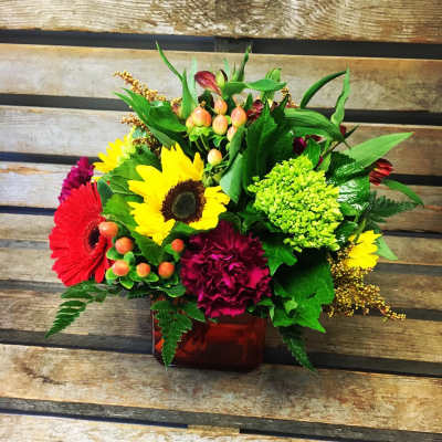 Mixed bouquet with sunflowers, gerbera daisies, and carnations in a red vase