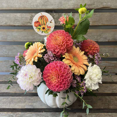 Fall floral arrangement in a white pumpkin container with colorful blooms and a pumpkin pick