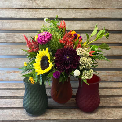 Three colorful flower arrangements in textured vases on a wooden bench