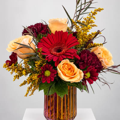 Mixed bouquet of red and peach flowers in an amber glass vase