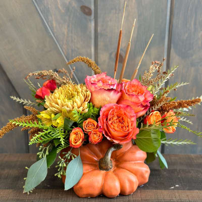 Orange pumpkin container with pink and orange flowers and dried accents