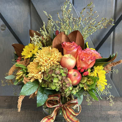 Autumn bouquet with yellow chrysanthemums, pink roses, and apples in a glass vase