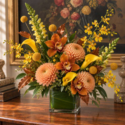 Arrangement of peach mums, yellow calla lilies, and orchids in a glass vase