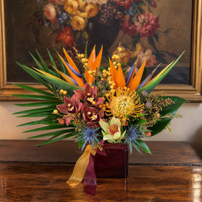 Tropical flower arrangement in a burgundy vase with orange and purple blooms