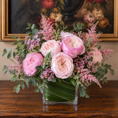 Pink roses arranged in a square glass vase with small purple flowers