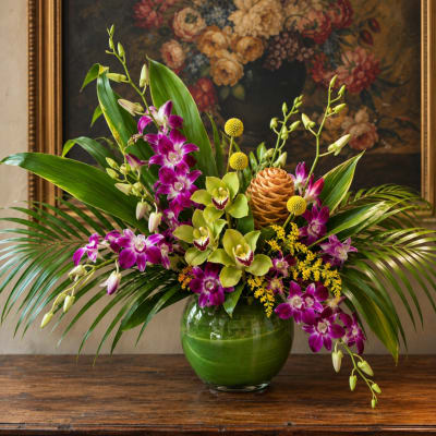 Purple and green orchid arrangement in a round glass vase