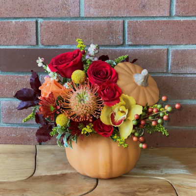 Fall floral arrangement in a pumpkin container with red roses and yellow orchid