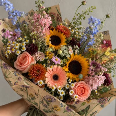 Mixed bouquet with sunflowers, roses, and daisies wrapped in floral paper