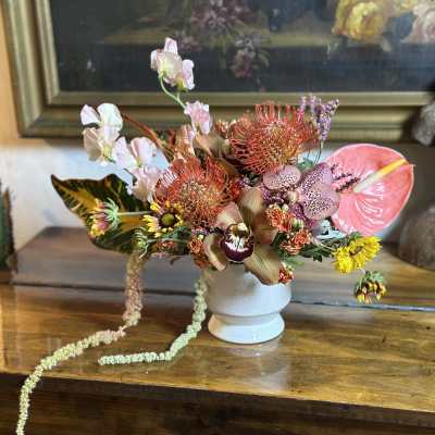 Tropical floral arrangement in a white vase with pink anthurium and orchids
